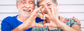 2 pessoas idosas fazem um coração com as mãos