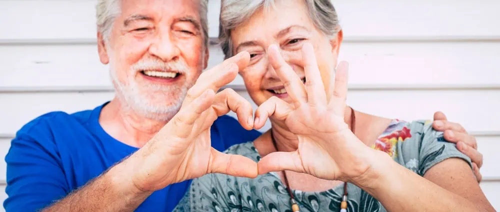 2 pessoas idosas fazem um coração com as mãos