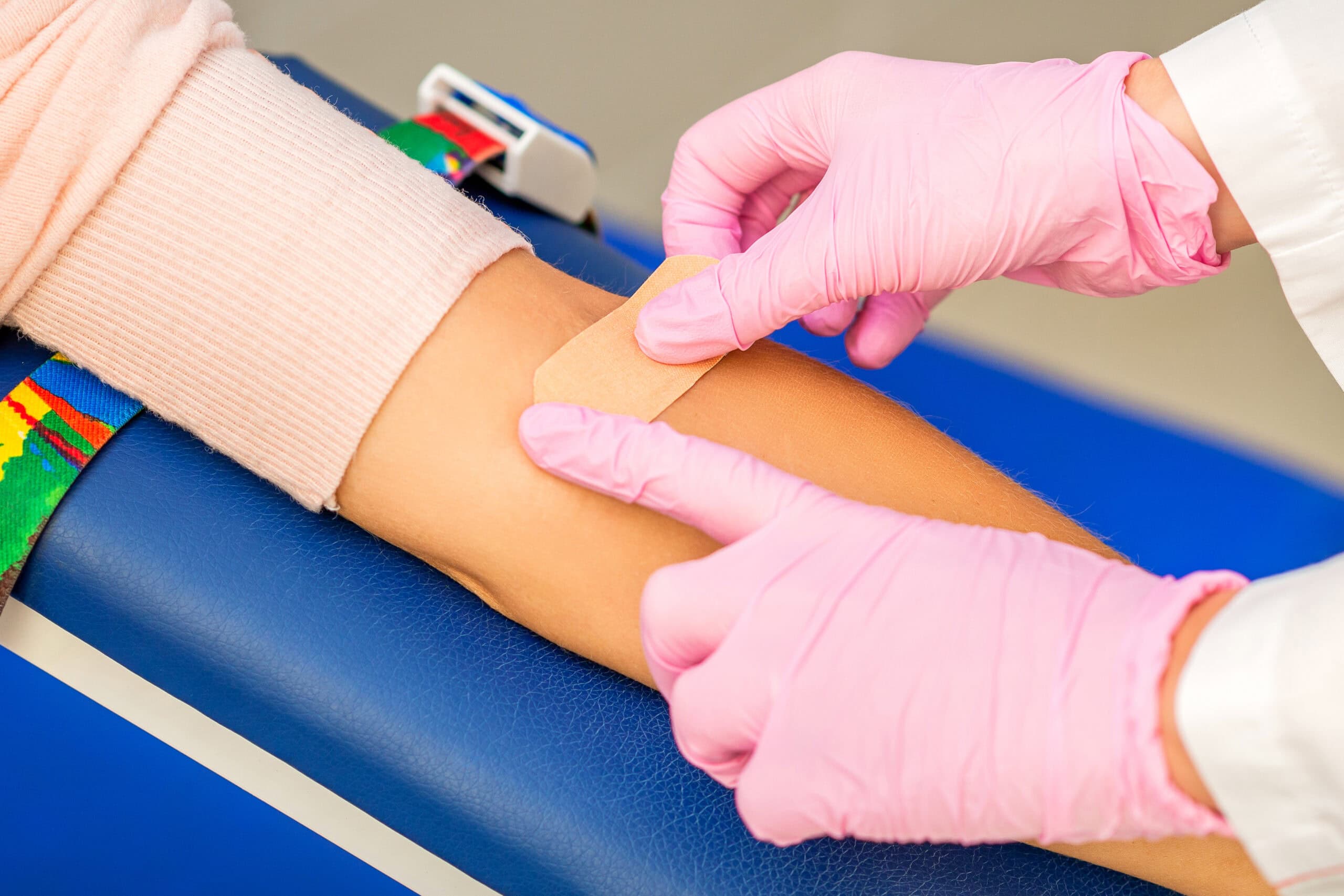 Uma pessoa com luvas rosas coloca um curativo no braço de outra pessoa após a coleta de sangue.