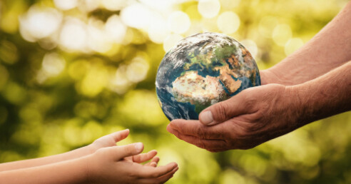 Mãos de uma pessoa idosa com o planeta terra em miniatura nas mãos entrega o planeta a uma criança. Uma das premissas da sustentabilidade é cuidar do planeta de forma que as próximas gerações tenham qualidade de vida