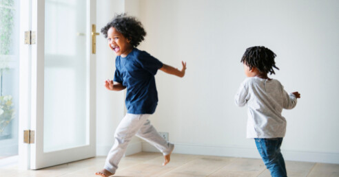 2 crianças brincam correndo dentro de casa