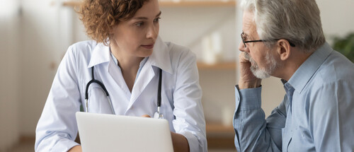 Médica atendendo paciente idoso de óculos e blusa azul