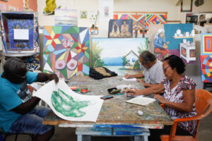 pessoas sentadas desenhando e ao fundo quadros de arte coloridos