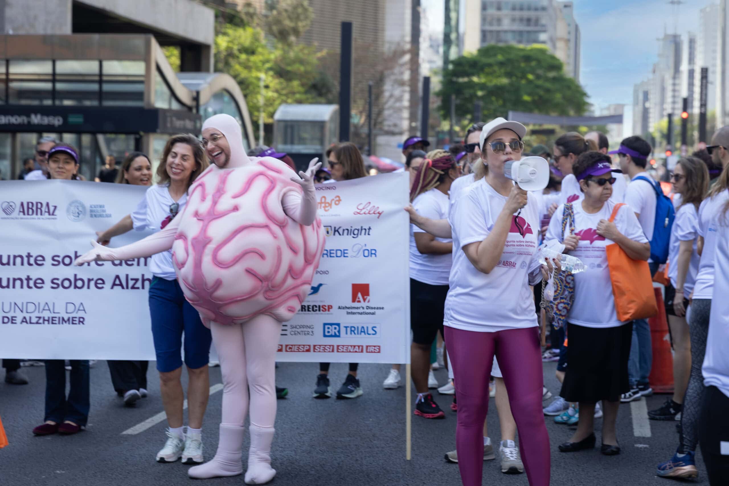 pessoas caminhando com banner, megafone e pessoa caracterizada de cérebro