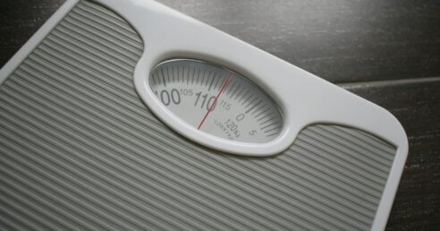 A imagem mostra uma balança de peso corporal branca e cinza, com o ponteiro apontando 113 kilos.