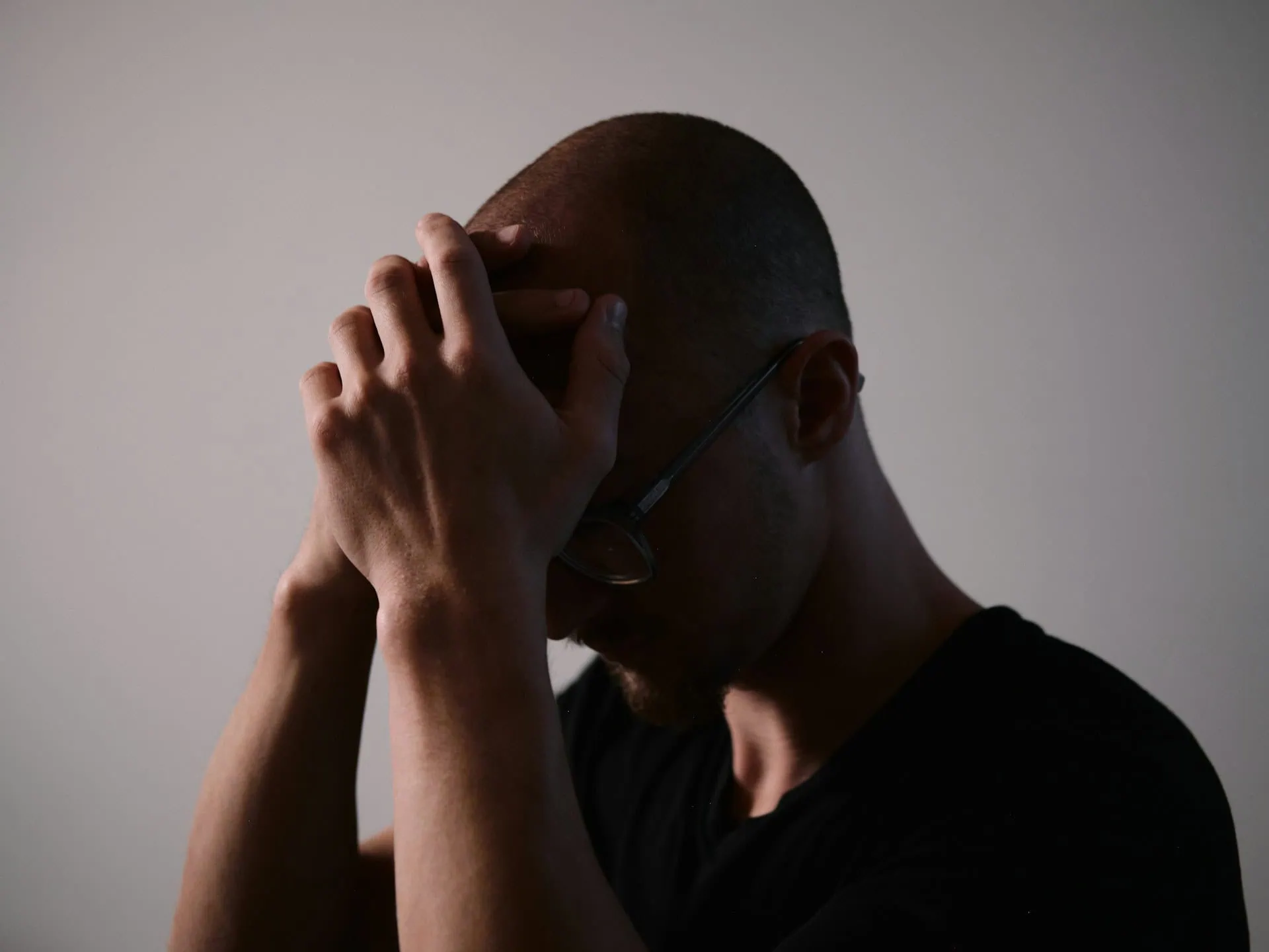 Homem com as duas mãos no alto da cabeça, logo acima da testa, indicando possível dor de cabeça ou preocupação.&nbsp;