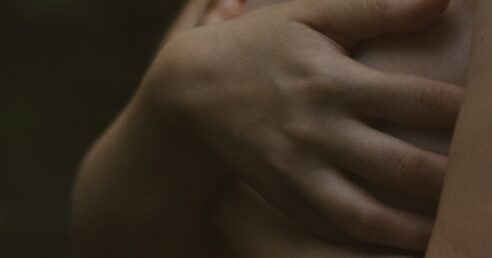 Fotografia em close mostra mulher de lodo, cobrindo os seios com as mãos.