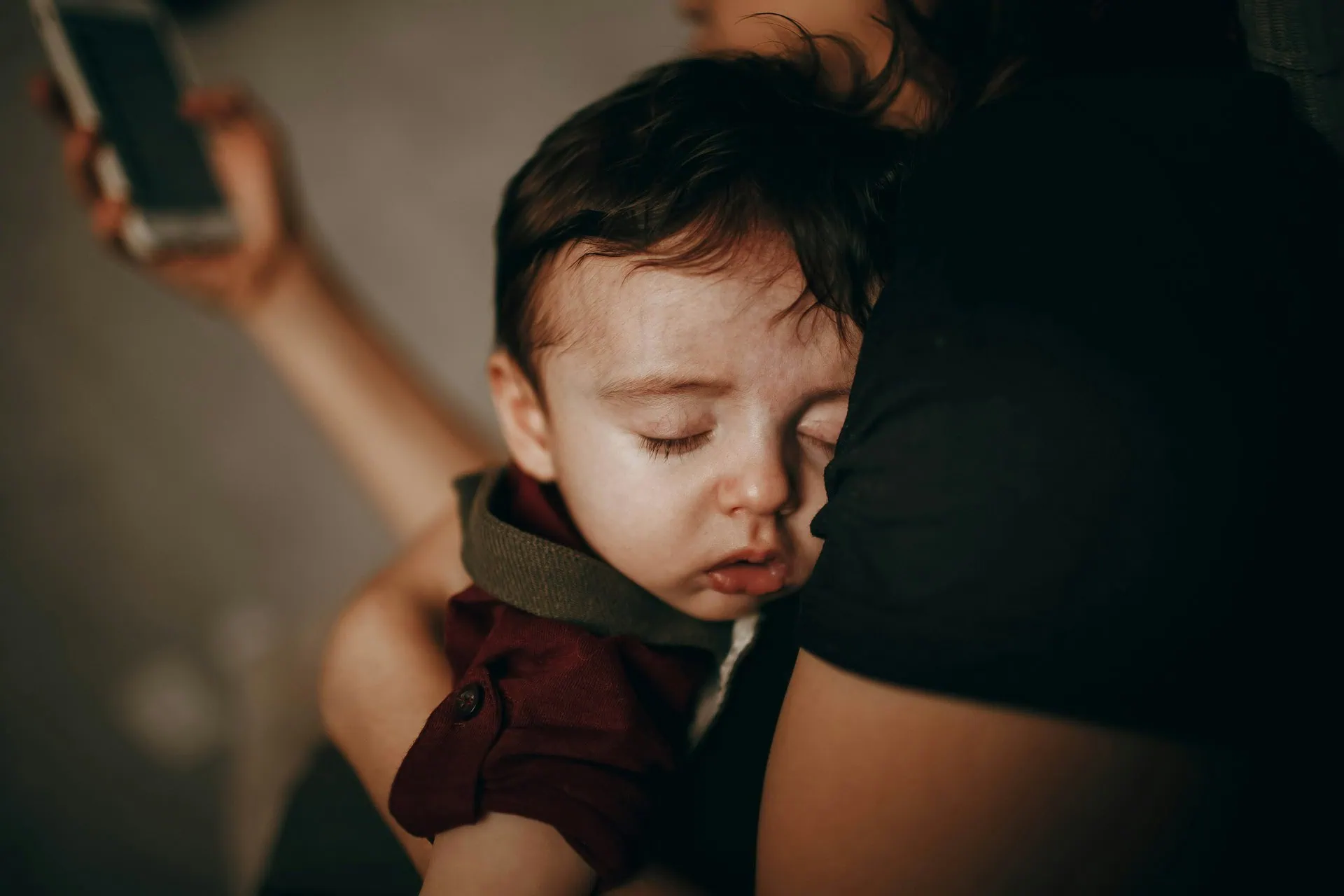 Mãe de blusa preta segurando um bebê num braço e no outro segurando um celular e fazendo uma ligação.