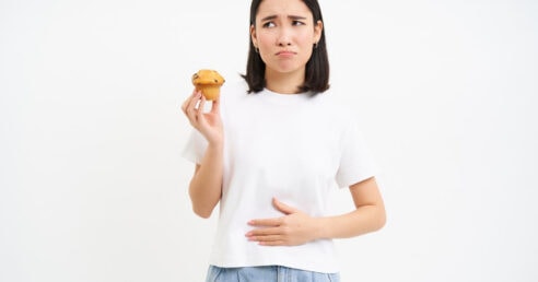 Mulher sentindo dor e desconforto ao comer um bolinho.
