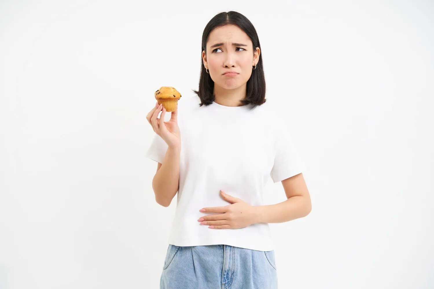 Mulher sentindo dor e desconforto ao comer um bolinho.