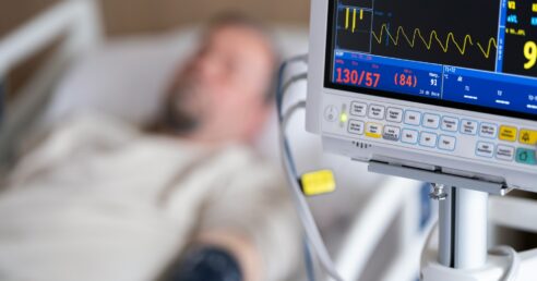 Imagem mostrar um homem deitado em uma cama de hospital ao lado de um monitor cardíaco.