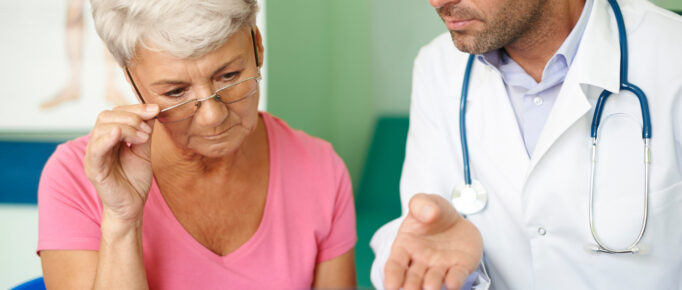 ALT: um jovem médico analisando um exame de imagem junto de sua paciente, uma mulher mais velha, olhando atentamente o exame.