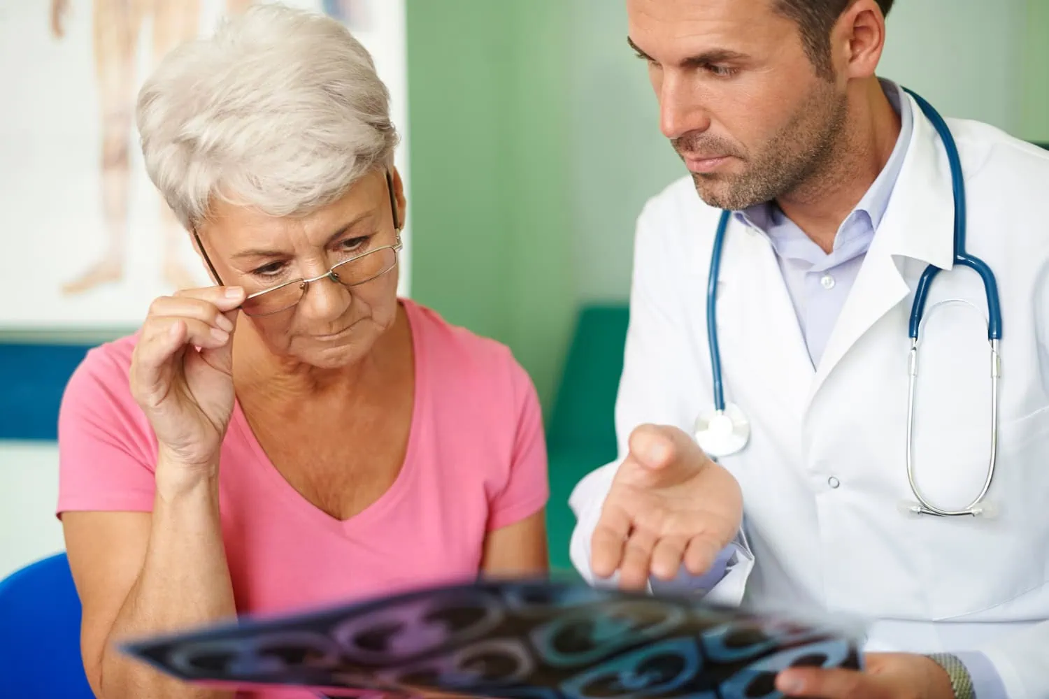 ALT: um jovem médico analisando um exame de imagem junto de sua paciente, uma mulher mais velha, olhando atentamente o exame.