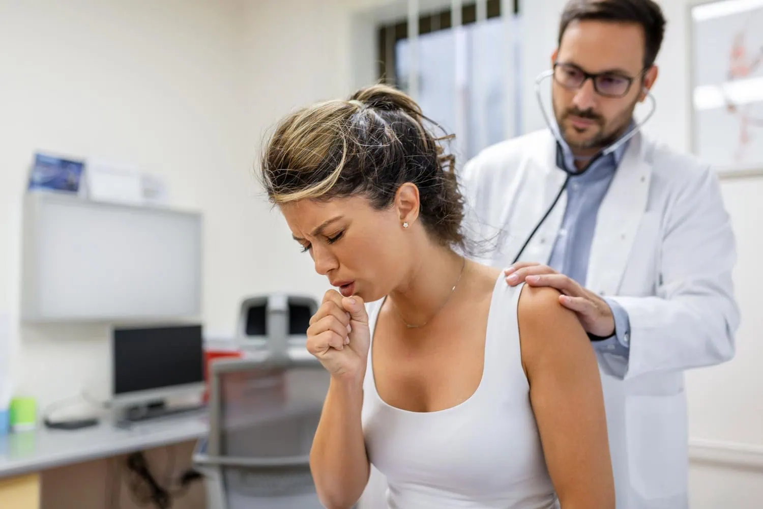 827 ALT: mulher jovem paciente em uma clínica. Ela está tossindo e o médico está realizando a ausculta pulmonar com o estetoscópio.